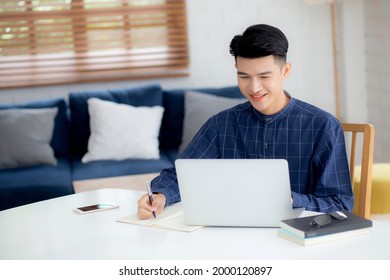 Young Asian Business Man Writing On Notebook For Planning Working And Using Laptop Computer On Desk At Home, Notes About Finance, Male Study And Learning, Business And Communication Concept.