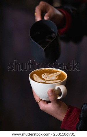 Young asian business woman barista wearing apron pouring hot milk into hot espresso black coffee for making latte art in his coffee shop, Latte Art training school concept. 
