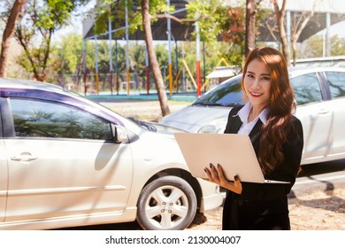 Young asian business woman in charge helps in car insurance during a car crash using state-of-the-art laptop computers to check and make accident claims with pleasure : Car insurance concept