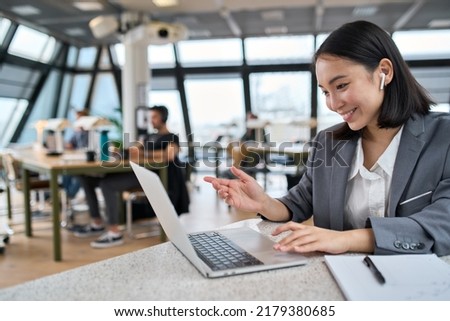 Young Asian business woman employee or executive manager using computer looking at laptop and talking leading hybrid conference remote video call virtual meeting or online training working in office.
