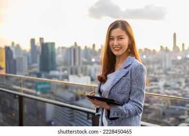 Young Asian business woman in formal suit with digital tablet standing outside the skyscraper building for real estate, housing and urban development - Shutterstock ID 2228450465
