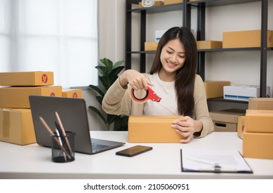 Young asian business woman packing product sealing cardboard with duct tape. Startup Small business owner entrepreneur packing product in the box delivery to customer working at home.