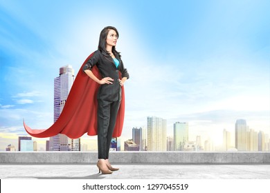 Young Asian Business Woman With Red Cape Standing On The Rooftop With Cityscapes Background