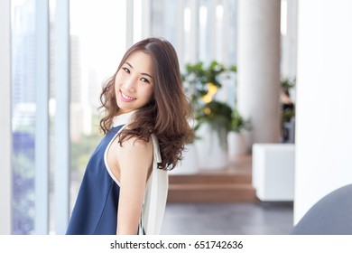 Young Asian business woman standing beside the window while looking to the camera (working woman or first jobber concept)