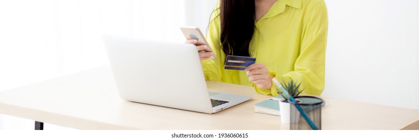 Young Asian Business Woman Using Smart Phone And Holding Credit Card While Online Shopping And Payment Online With Laptop Computer On Desk At Home, Female Holding Debit Card, Communication Concept.