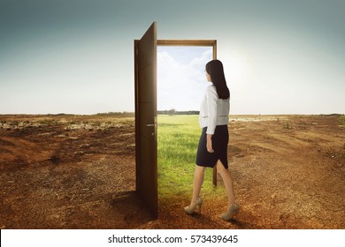 Young Asian Business Woman Walking To The Open Door Going To Green Environment On Cracked Land Background