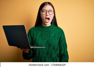 Young Asian Business Woman Wearing Glasses And Working Using Computer Laptop Angry And Mad Screaming Frustrated And Furious, Shouting With Anger. Rage And Aggressive Concept.