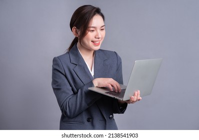 Young Asian Business Woman Wearing Suit And Using Laptop On Gray Baclground