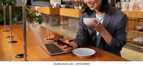 Young Asian business woman wearing suit drinking coffee using smartphone in cafe. Happy smiling female professional working holding mobile phone using smartphone texting messages on cellphone. - Powered by Shutterstock