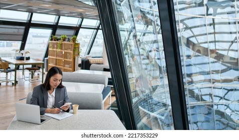 Young Asian business woman wearing suit working in big modern office space. Female korean company manager, professional worker entrepreneur or employee using smartphone and laptop at workplace.