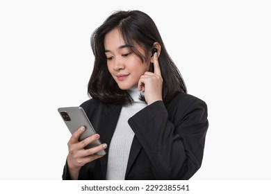 A young Asian business women on isolated white background, a women in a black suit, holding a mobile and her ear, using ear buds.