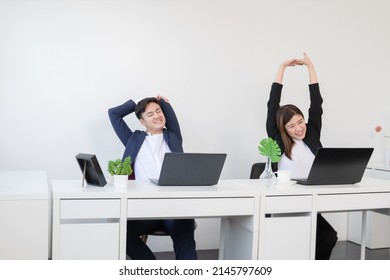 Young Asian Businessman And Businesswoman Relaxing Stretching Arms, Head And Hands After Work With Laptop For A Long Time At Office. Business People Wear Formal Suit Stretch Oneself On Break Time