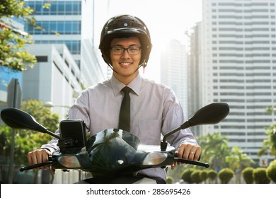 Young Asian Businessman Commuting To Job. The Man Rides A Motorcycle Scooter With White Helmet And Smiles At Camera