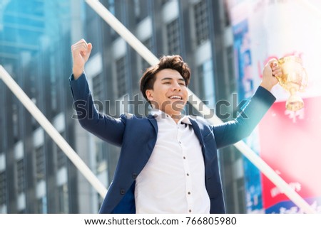 Young Asian businessman is holding golden trophy with big smile