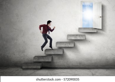 Young Asian businessman jumping on the staircase toward an opportunity door with bright sunlight
