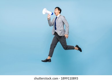 Young Asian businessman jumping and shouting on megaphone isolated on light blue color background