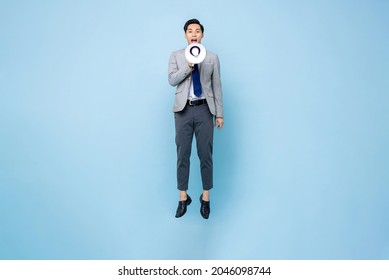 Young Asian businessman jumping and shouting on megaphone isolated on light blue background
