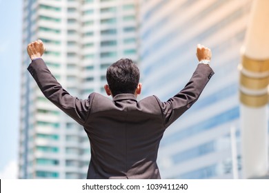 Young Asian Businessman Standing Outdoor With City Background, Successful Man In Suit With Arms Up Celebrating In Modern Building Center. Business Success And Target Concepts