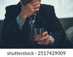 Young Asian businessman stressed from drinking alcohol, depressed man alone drinking on the couch at home, alcohol addiction treatment, alcohol addiction problem