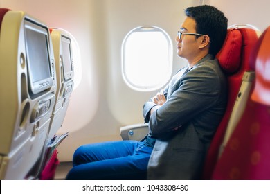 Young Asian Businessman With Suits Sitting On Seat In Airplane Near The Window And Sleeping With Relaxing