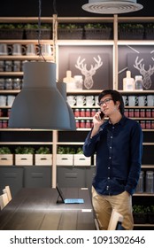 Young Asian Businessman Using Smartphone For Business Talk Looking At His Digital Tablet In Co Working Space. Freelance Lifestyle Or Digital Nomad Concepts