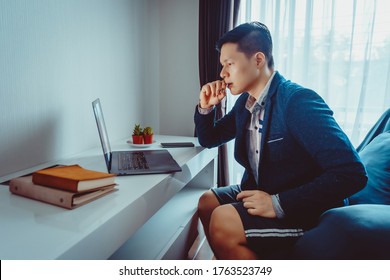 Young Asian Businessman Wear Formal Suit With Short Pants Having Video Conference Meeting With Business Partner On Sofa At Home In Living Room During Quarantine Period.