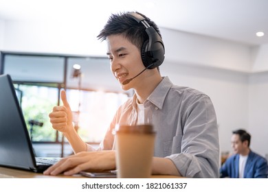 Young Asian businessman wearing headphones studying online,   webinars on their laptop, listening and  meeting sitting at their desks