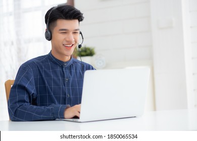 Young Asian Businessman Working On Laptop Computer Wearing Headphone At Home, Business Man Wearing Headset For Video Conference, Communication And Education, Male Study And Learning For E-learning.