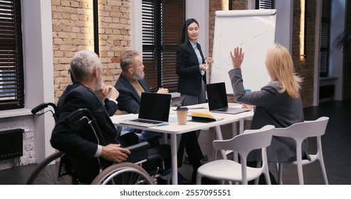 Young Asian businesswoman discusses statistical data standing by whiteboard. Diverse businesspeople discuss growth strategies in corporate office - Powered by Shutterstock