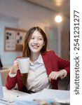 Young asian businesswoman is drinking coffee while working late at night in a modern office, enjoying a moment of relaxation during her busy workday