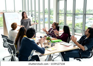 Young asian businesswoman explain idea to group of creative diverse team at modern office. Manager standing against rear view of multiethnic people. Audience applauding speaker after presentation. - Powered by Shutterstock