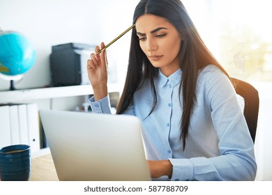 Young Asian Businesswoman Frowning With Concern As She Tries To Understand Something She Is Reading On Her Laptop Computer Scratching Her Head With Her Pencil In Perplexity