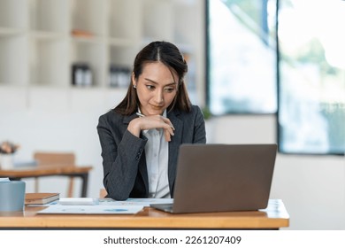 Young Asian businesswoman holding a pen sitting and analyzing the details of management information Finance is happy at the desk in the office. - Shutterstock ID 2261207409