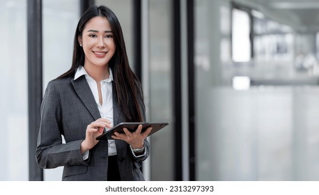 Young Asian businesswoman looking at camera holding  tablet at office. - Powered by Shutterstock