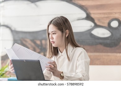 Young Asian Businesswoman Reading Paper At Her Workplace In Office