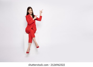 Young Asian businesswoman in red suit sitting and pointing to empty copy space isolated on white background