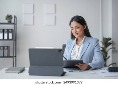 Young asian businesswoman reviewing notes on a clipboard and working on a tablet, smiling at something on the screen - Powered by Shutterstock