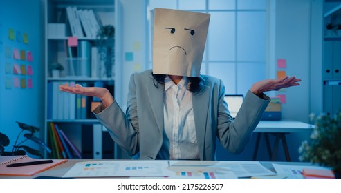 Young Asian businesswoman sit on desk wear draw sad mask paper craft bag feel bad mood with fail work project in office at night. Anonymous lady mad and confuse with overwork, Work mental health. - Shutterstock ID 2175226507