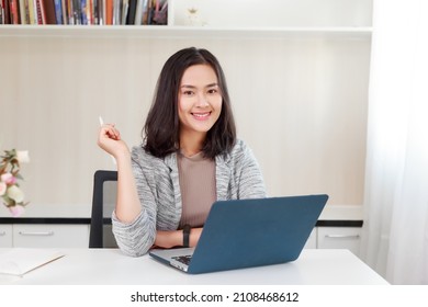 Young Asian Businesswoman Sitting In Front Of Computer During Work At Home. Happy Friendly Asian Woman Looking At Camera With Smiley Face. Business And Technology, Home Office, Lifestyle Concept.