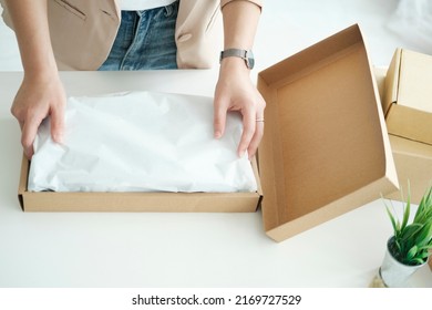 Young Asian businesswoman startup entrepreneur SME owner picking up a yellow shirt before packing it in an inner box with a customer. Online Business Ideas and Freelance.