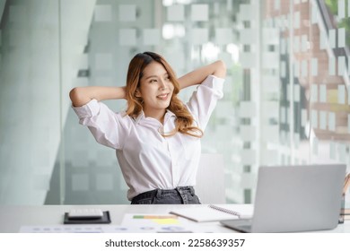 Young Asian businesswoman stretches her arms and closes her eyes to relax tired muscles from working at the desk all day at the office. - Powered by Shutterstock