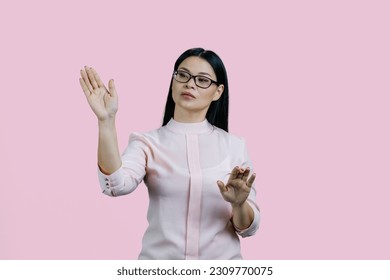 Young asian businesswoman is swiping an invsible touch screen. Isolated over pink background. - Powered by Shutterstock