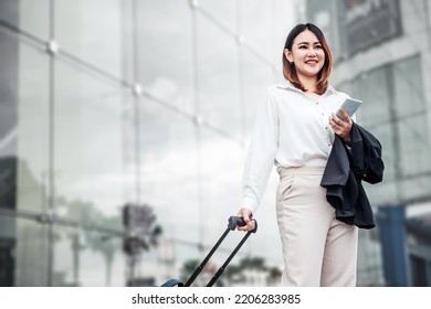 Young Asian Businesswoman Talking On Phone And Walking In Airport Before Business Trip. Beautiful Woman Passenger Has Mobile Call And Discusses Something With Smile, Holds Coffee In Hand