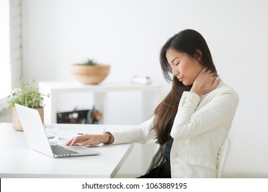 Young Asian Businesswoman Touching Massaging Stiff Neck To Relieve Pain In Muscles After Sedentary Computer Work In Incorrect Posture, Japanese Or Chinese Woman Suffering From Fibromyalgia At Work