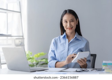 Young Asian businesswoman using a calculator to calculate business principles. Accounting statistics concept at the office. - Shutterstock ID 2366156887