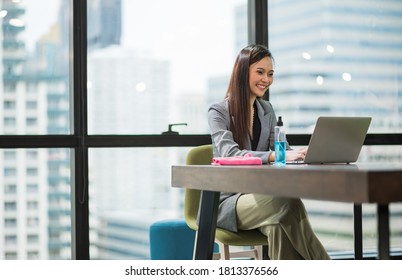 Young Asian Businesswoman Using Laptop Sitting In Modern Office Working With Social Distancing Alcohol Gel On Desk.