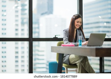 Young Asian Businesswoman Using Laptop Sitting In Modern Office Working With Social Distancing Alcohol Gel On Desk.