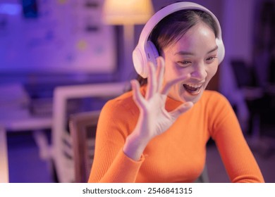 Young asian businesswoman wearing headphones is making ok sign with fingers while working late at night in home office using laptop computer, showing approval and satisfaction - Powered by Shutterstock