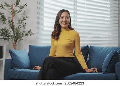 Young asian businesswoman wearing a yellow turtleneck sweater is sitting on a sofa and smiling - Powered by Shutterstock