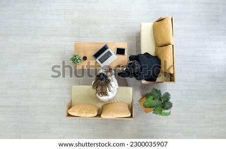 Young asian businesswoman in white suit and senior manager meeting in modern coworking space. Flower pot, coffee cup, laptop and and tablet computer are on wooden table. Top view